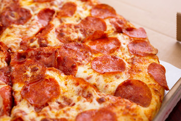 A closeup view of a standard pepperoni pizza pie, inside a pizza box, in a restaurant or kitchen setting.