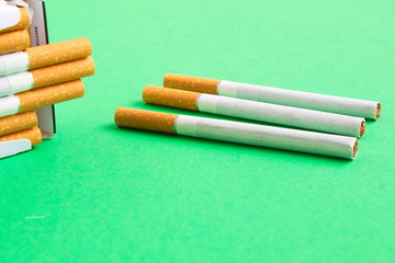 three loose cigarettes next to a pack on green table