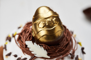 Easter cake decorated by golden chocolate egg on white wooden background, Traditional Kulich, Paska  ready for celebration