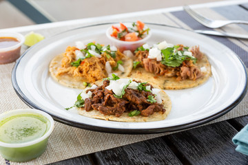 A view of three Mexican street tacos on a plate, in a restaurant or kitchen setting.