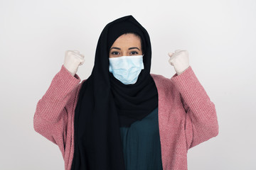 Waist up portrait of strong successful determined young female winner in casual t-shirt raising arms, clenching fists, exclaiming with joy and excitement. Victory, success and achievement concept.