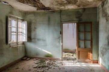 Habitación verde con puerta abierta iluminada por una ventana en casa abandonada.