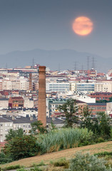 Paisaje urbano de la ciudad de Terrassa al anochecer con la luna llena (Cataluña, España).