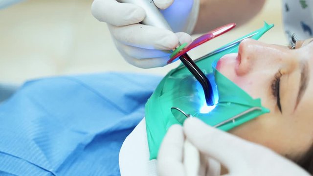 A doctor treats a tooth with a photopolymer lamp. The procedure for filling a tooth in a clinic.