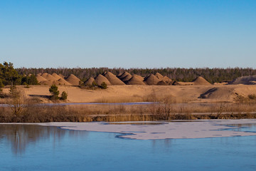 A spring lanscape of golden sand, evergreen trees, a reflecting still half frozen river and...