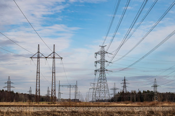 A spring landscape of several spring metal construction pylons with high voltage powerlines running above the nature under the dramatic cloudy blue sky