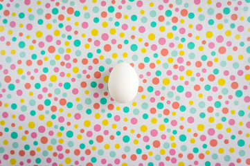 A simple white egg on a background of multi-colored polka dots.