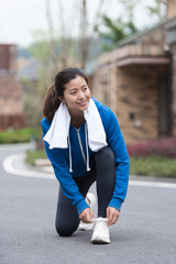 A young Asian woman squatting to tie shoelaces