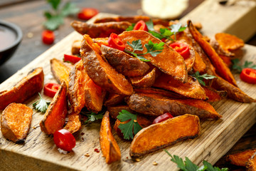 Healthy Baked Orange Sweet Potato wedges with dip sauce, herbs, salt and pepper on wooden board