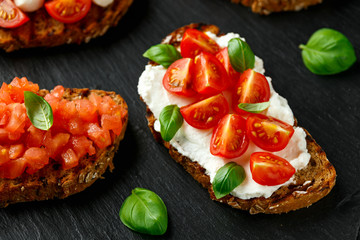 Bruschetta with ricotta, mozzarella cheese, basil, cherry and sliced tomatoes on rustic stone board