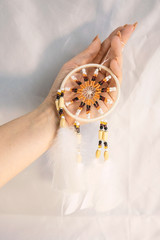 Dream catcher in female woman hand on satin, handmade native american of yellow blue beads with white feathers. Bad dreams protection. Concept peaceful, peace of mind, meditation, tranquility