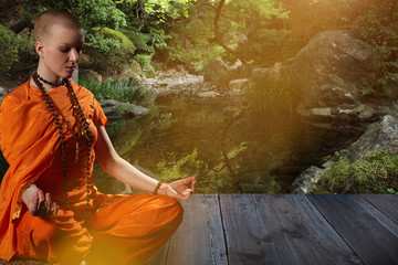 Beautiful young woman in orange robe sits in meditation on the background of the zen...