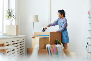 Side view portrait of young Asian woman packing cardboard boxes and smiling happily while moving to...