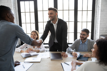 Smiling successful businessman in suit shaking hand of african american business partner at company...