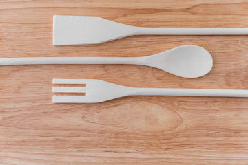 A white wooden spoon, a spatula and a spatula with cloves lie next to each other on a light brown wooden board with stains. Amazing background for a cafe or restaurant menu, signboard.