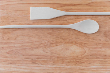 White wooden spoon and spatula lie next to each other on a light brown wooden board with stains. Amazing background for a cafe or restaurant menu, signboard.
