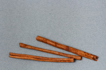 Three sticks of cinnamon on texture gray background. Isolated ingredients. Top view