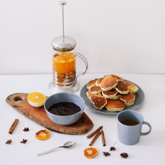 Lush pancakes and teapot with spices, cup of tea with orange, cinnamon, anise. Tasty breakfast on white background. Good morning
