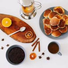 Lush pancakes and teapot with spices, cup of tea with orange, cinnamon, anise. Tasty breakfast on white background. Good morning