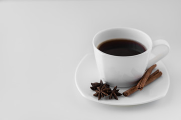 White cup with coffee and saucer, with three star anise star anise and cinnamon sticks, on a white background. A good idea for the menu or sign of a restaurant or cafe, cafeteria