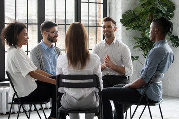 Happy handsome male mentor counselling speaking with diverse people sitting in circle at group therapy session. Business coach training staff, having fun, team building activity at work.
