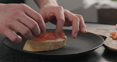 man hands making bruschetta with cream cheese and salted trout on black plate