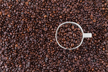 White mug with roasted coffee beans everywhere, inside the mug and a lot around it. Great for going to a cafe, restaurant, cafeteria menu or as a sign.