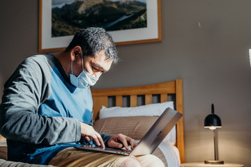 Fototapeta na wymiar Asian man weared medical mask. Sitting and using laptop in bedroom.