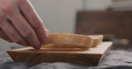 man hand put ciabatta slices on olive wood board closeup