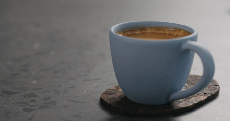 blue cup with fresh espresso on cork coaster on concrete surface