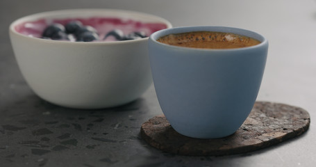 man hand put blue cup with fresh espresso and blueberry yogurt on concrete surface
