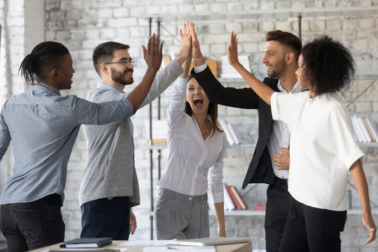 Excited successful multiracial business people giving high five, celebrating win. Good teamwork result concept. Happy employees team engaged in team building activity at corporate meeting.