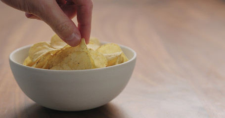 man hand take black pepper seasoned potato chips from white bowl on walnut wood table with copy space