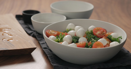 man hands put mozzarella balls in white bowl with kale leaves and tomatoes