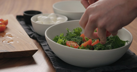 man hands put sliced cherry tomatoes in white bowl with kale leaves