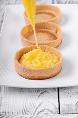 Shortbread tartlets are filled with lemon curd out of the pastry bag on the ceramic platter