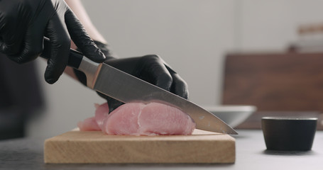 man hands in black gloves slicing turkey fillet on oak wood board