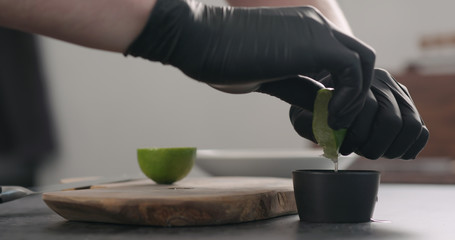 man hands in black gloves squeeze lime in black bowl