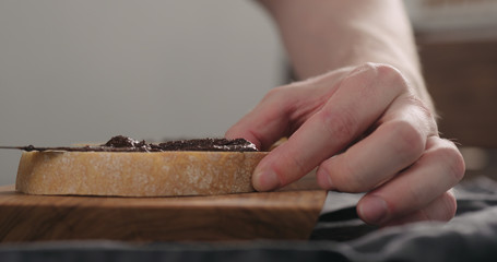 man spreading chocolate nut spread on ciabatta slice on olive board