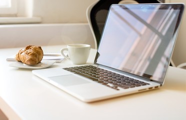 Laptop mockup on work desk in sunset. Close-up laptop with flowers, coffee, croissant, with morning light. Modern, thin laptop design.White. Isolated screen for mockup. Laptop profile. Home office