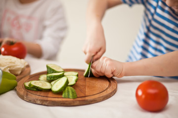 Obraz na płótnie Canvas Happy children prepares vegetables for salad in home kitchen. Healthy eating.