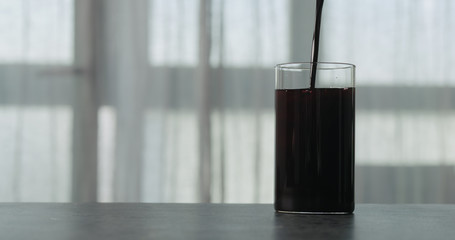 pour bilberry juice into water in glass on concrete countertop with window on background