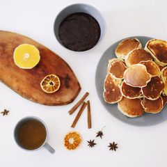 Lush pancakes and teapot with spices, cup of tea with orange, cinnamon, anise. Tasty breakfast on white background. Good morning
