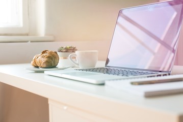 Laptop mockup on work desk in sunset. Close-up laptop with flowers, coffee, croissant, with morning light. Modern, thin laptop design.White. Isolated screen for mockup. Laptop profile. Home office