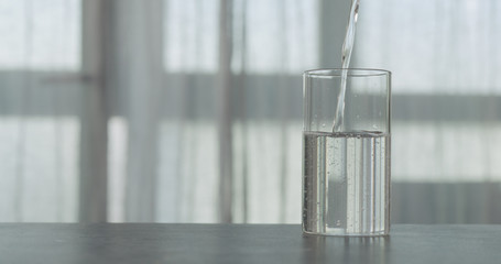 pour water into glass on concrete countertop with window on background