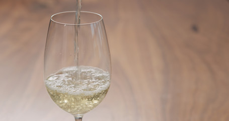 pour white wine in wineglass on walnut table