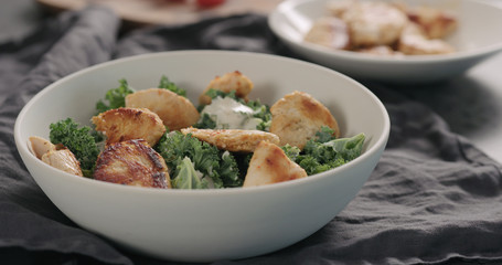 making caesar salad with kale and turkey in white bowl, add turkey