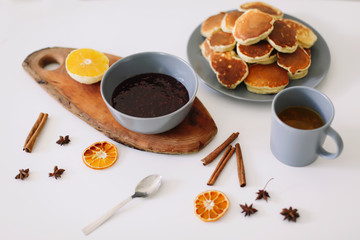 Lush pancakes and teapot with spices, cup of tea with orange, cinnamon, anise. Tasty breakfast on white background. Good morning