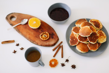 Lush pancakes and teapot with spices, cup of tea with orange, cinnamon, anise. Tasty breakfast on white background. Good morning