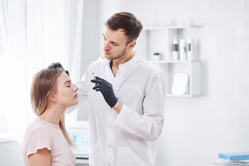 Obraz premium Beautician man gives beauty injections to young woman patient, handsome dermatologist puts disport in forehead wrinkles, face botox filler in the cosmetology salon
